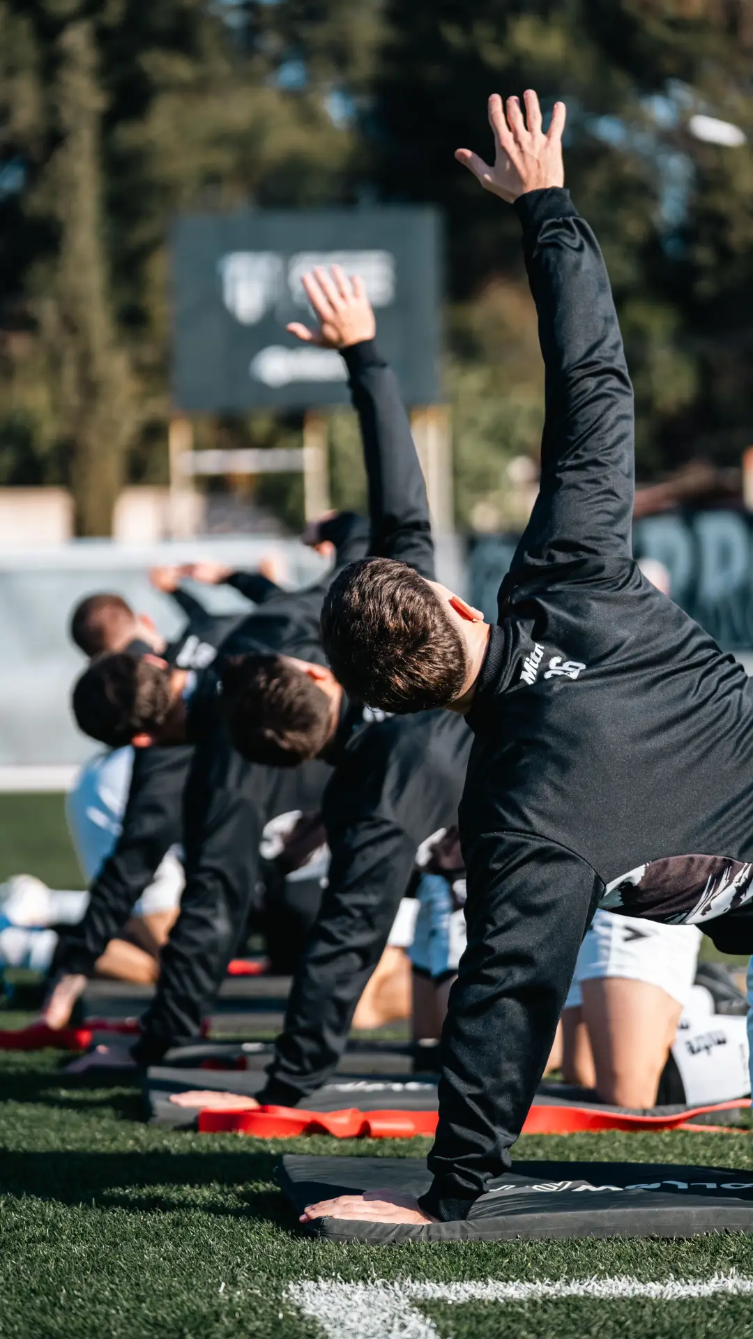 A group of athletes perform stretching exercises on a field