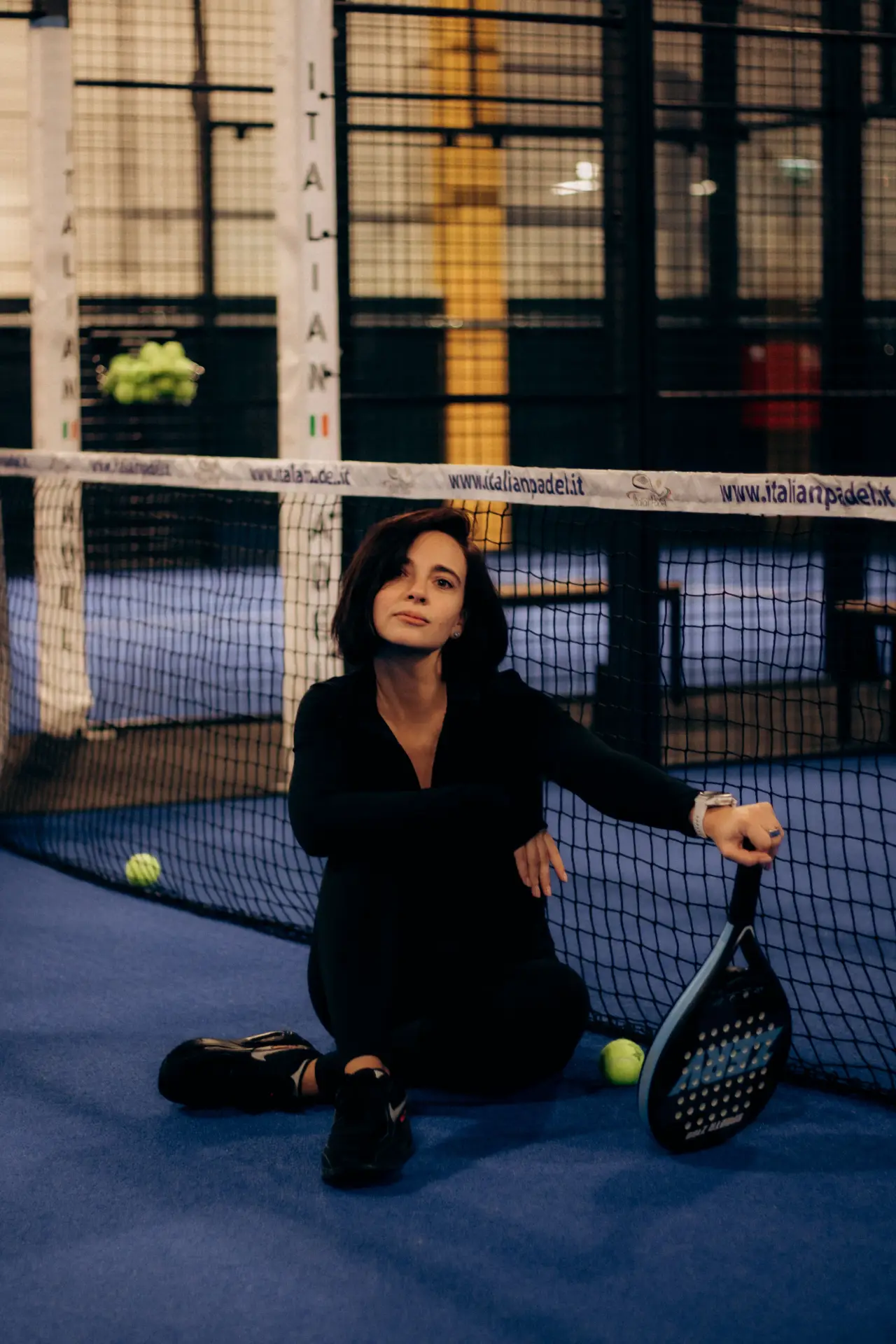 Young woman sitting on a blue padel court with a racket