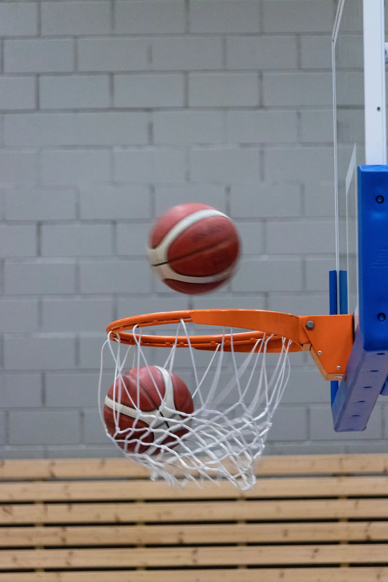 Two basketballs seen scoring through a hoop on an indoor